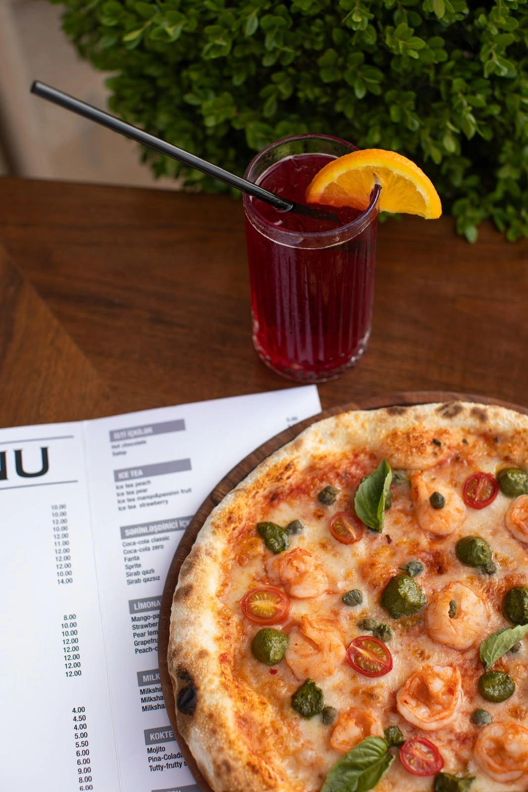 Pizza and a red drink with orange slices on a wooden restaurant table.