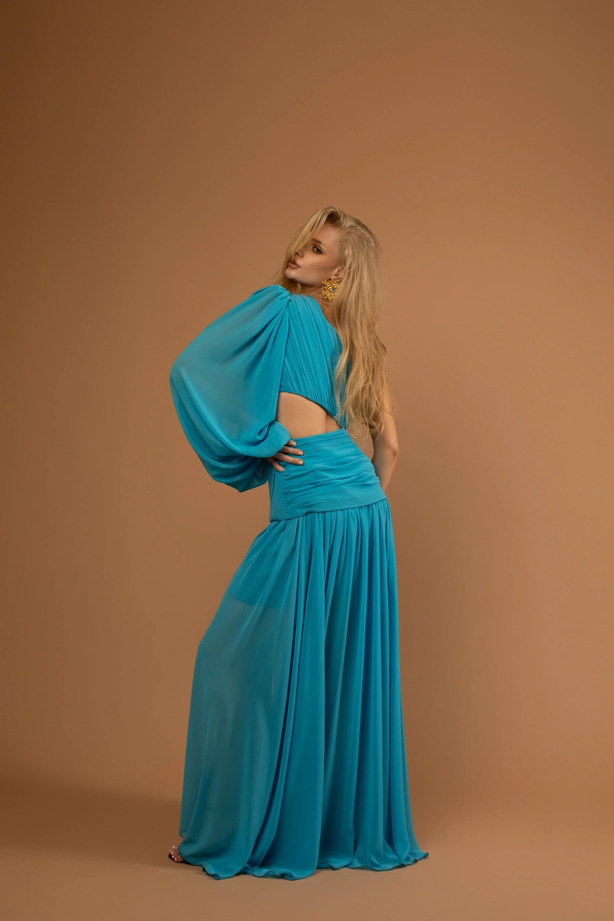 Full-length studio portrait of a woman in a flowing blue dress against a warm brown backdrop.