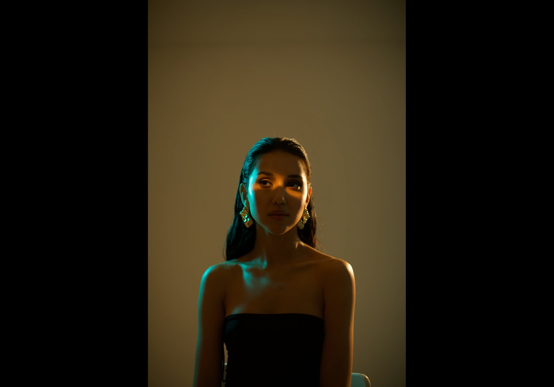 A woman in a black dress illuminated by warm and blue light in a dark studio.