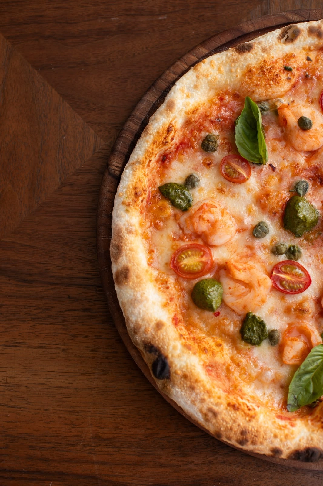 Close-up of a pizza topped with basil and cherry tomatoes on a wooden table.