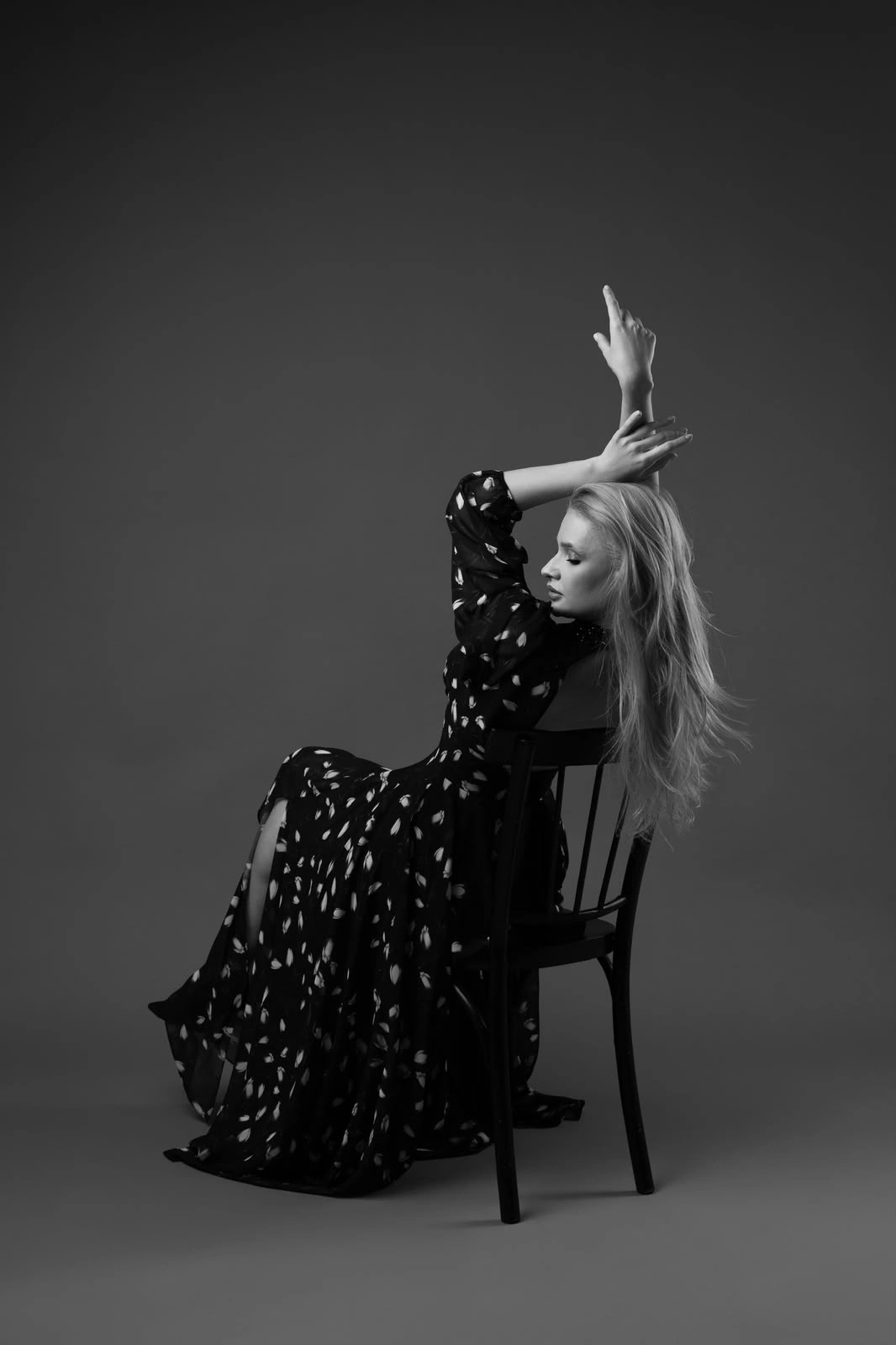 Black-and-white portrait of a woman sitting on a chair with one arm raised.