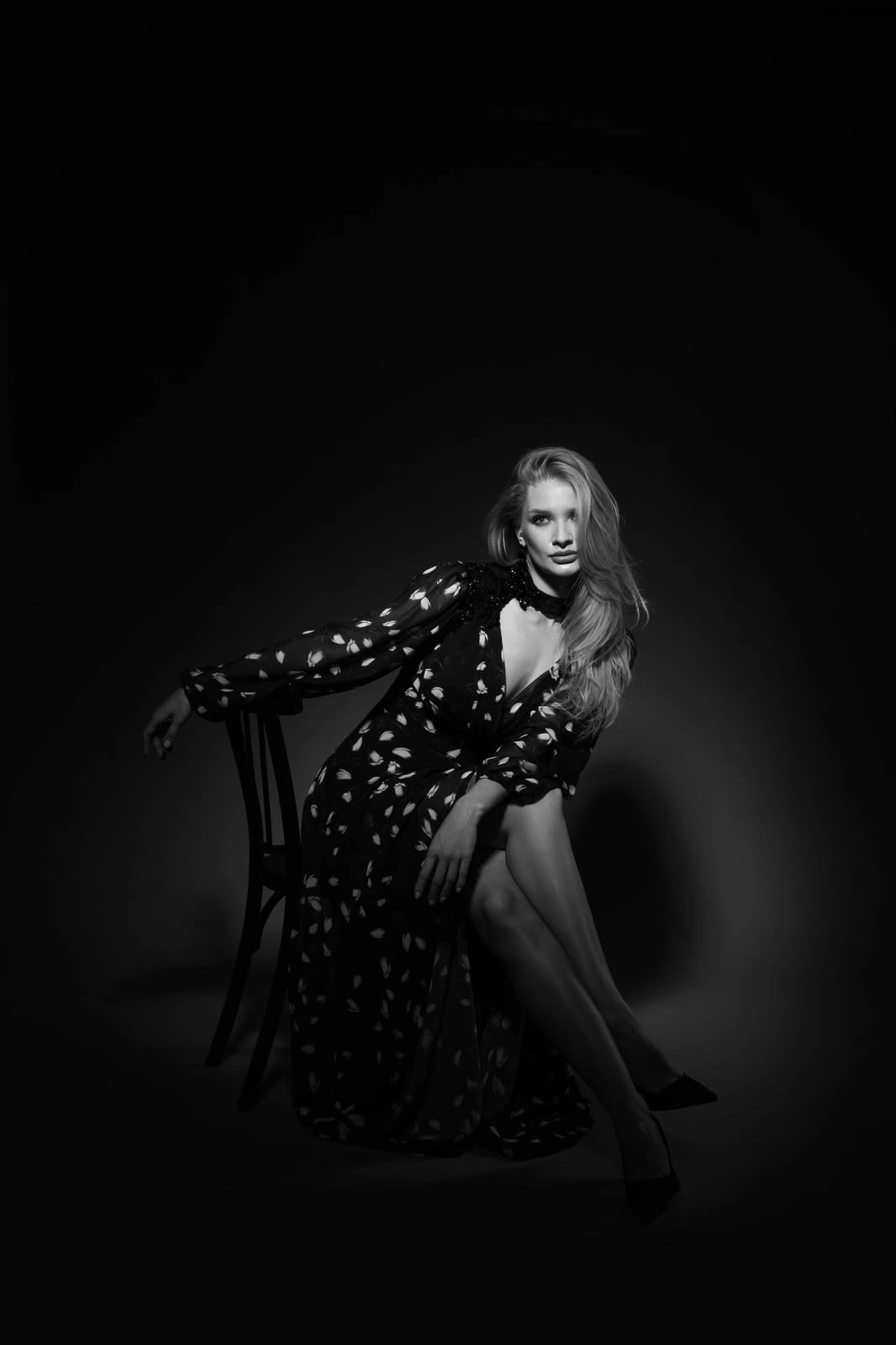 Black-and-white studio portrait of a woman in a patterned dress seated in a pool of light.