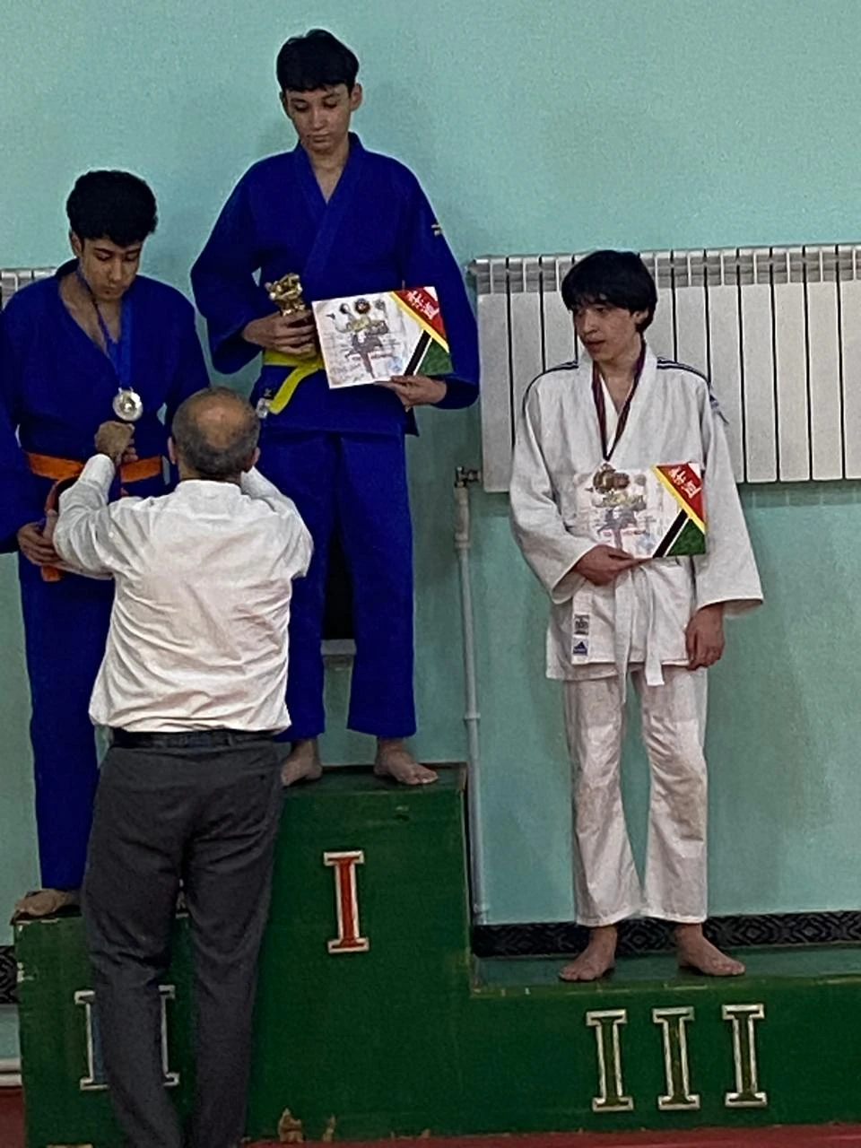 Zeyd Suleymanli on the third-place judo podium holding his certificate